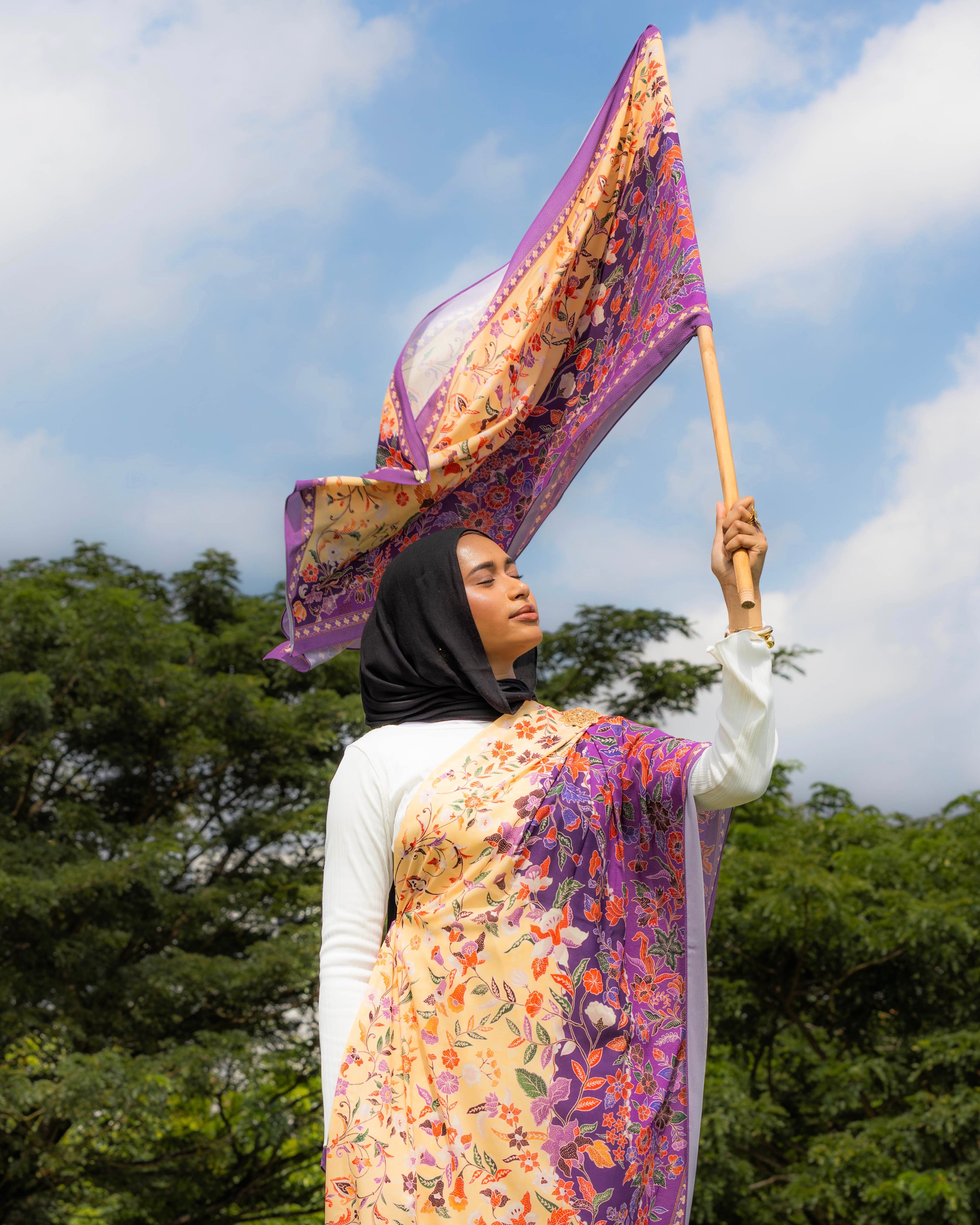 Woman wearing a Soof Sarung in Embun floral chiffon, purple and yellow headscarf.